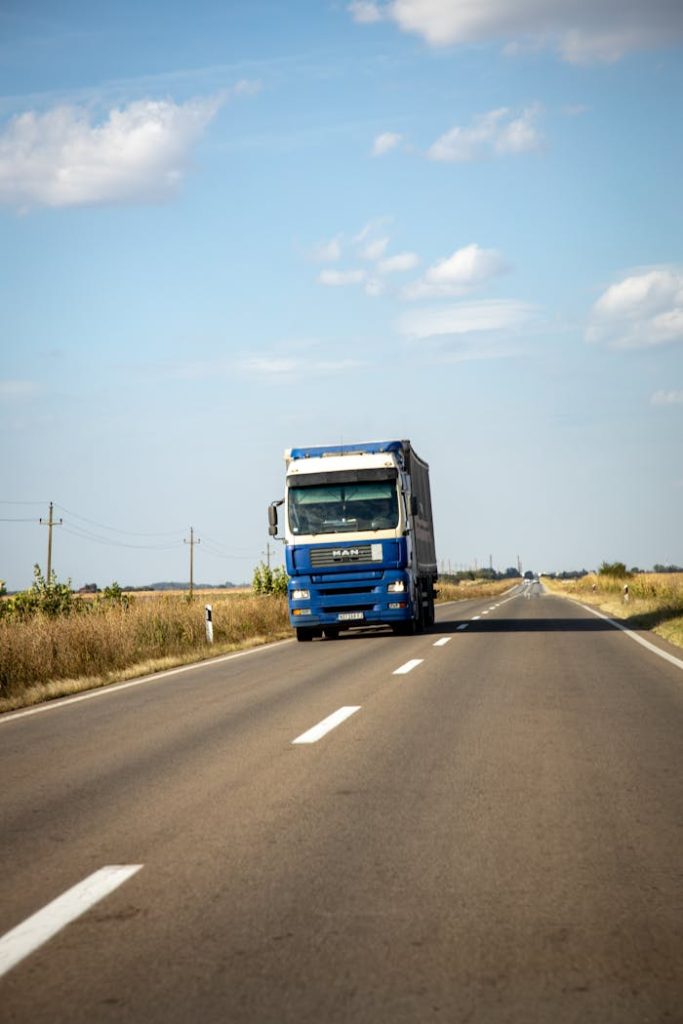 A blue truck drives along a rural road on a clear day, showcasing transportation and travel.
